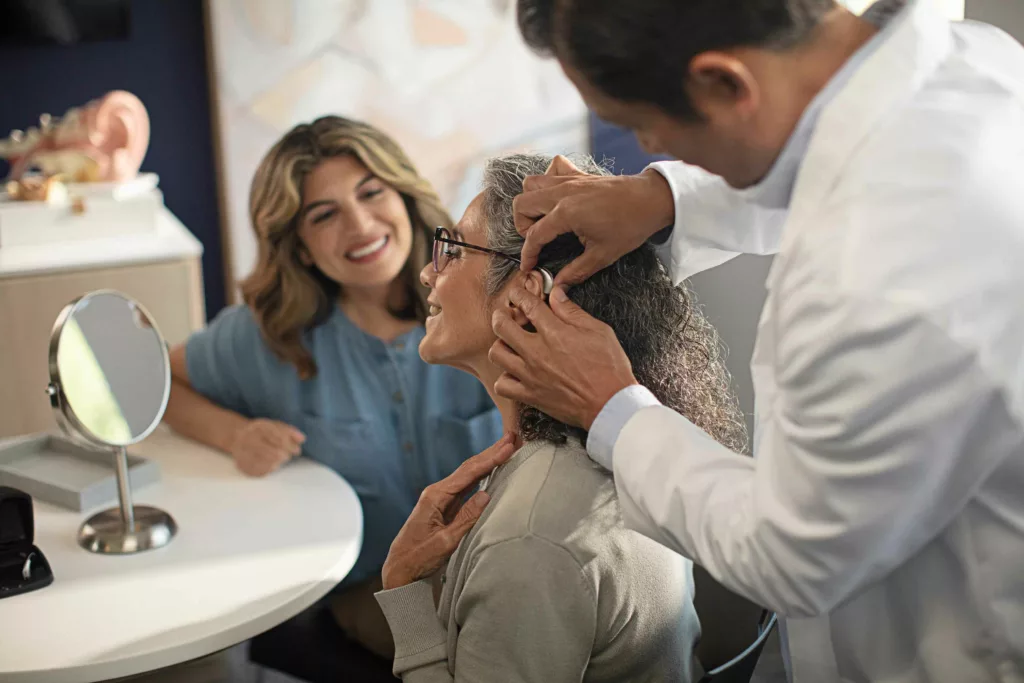 Hearing specialist examining patient's ear as they fit them for a behind-the-ear BTE hearing aid