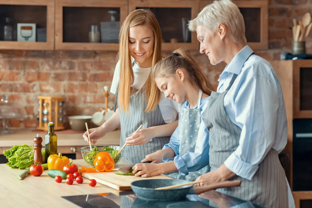 Middle aged woman and adult woman teach little girl to cook healthy