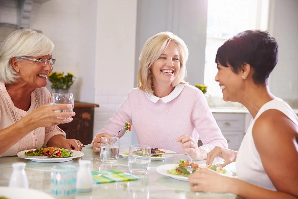 Smiling women eating salad at table