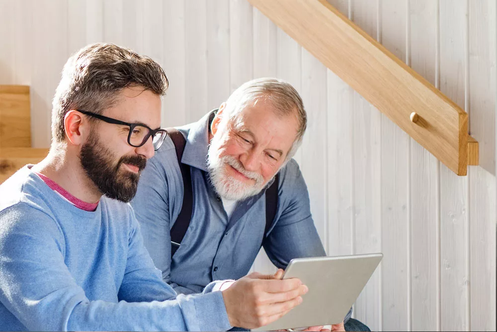 Smiling young man showing tablet to smiling senior men