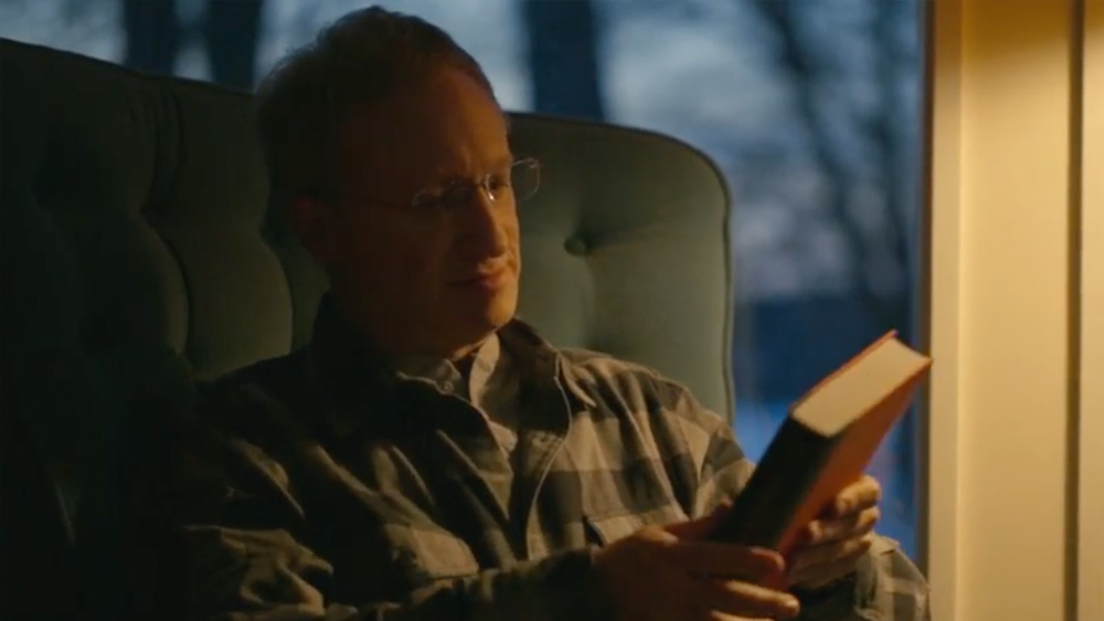 Elderly man sitting on his comfy chair, reading the back cover of a book