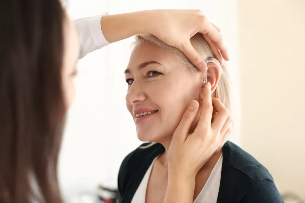 Otolaryngologist putting hearing aid in woman's ear