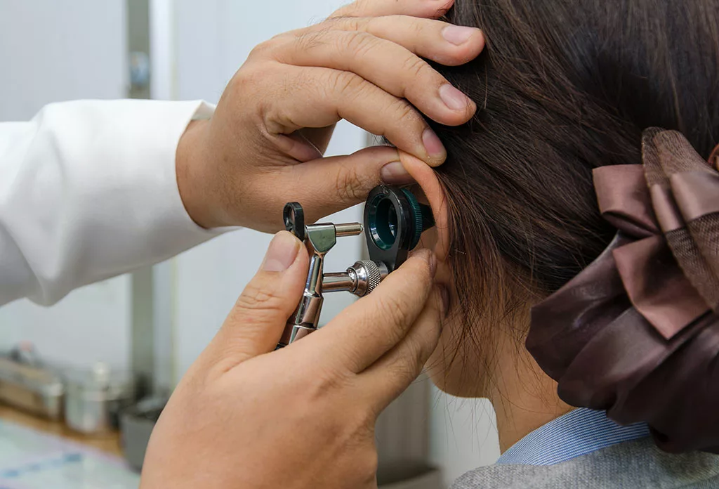 Doctor's hands using otoscope to examine a woman's ears