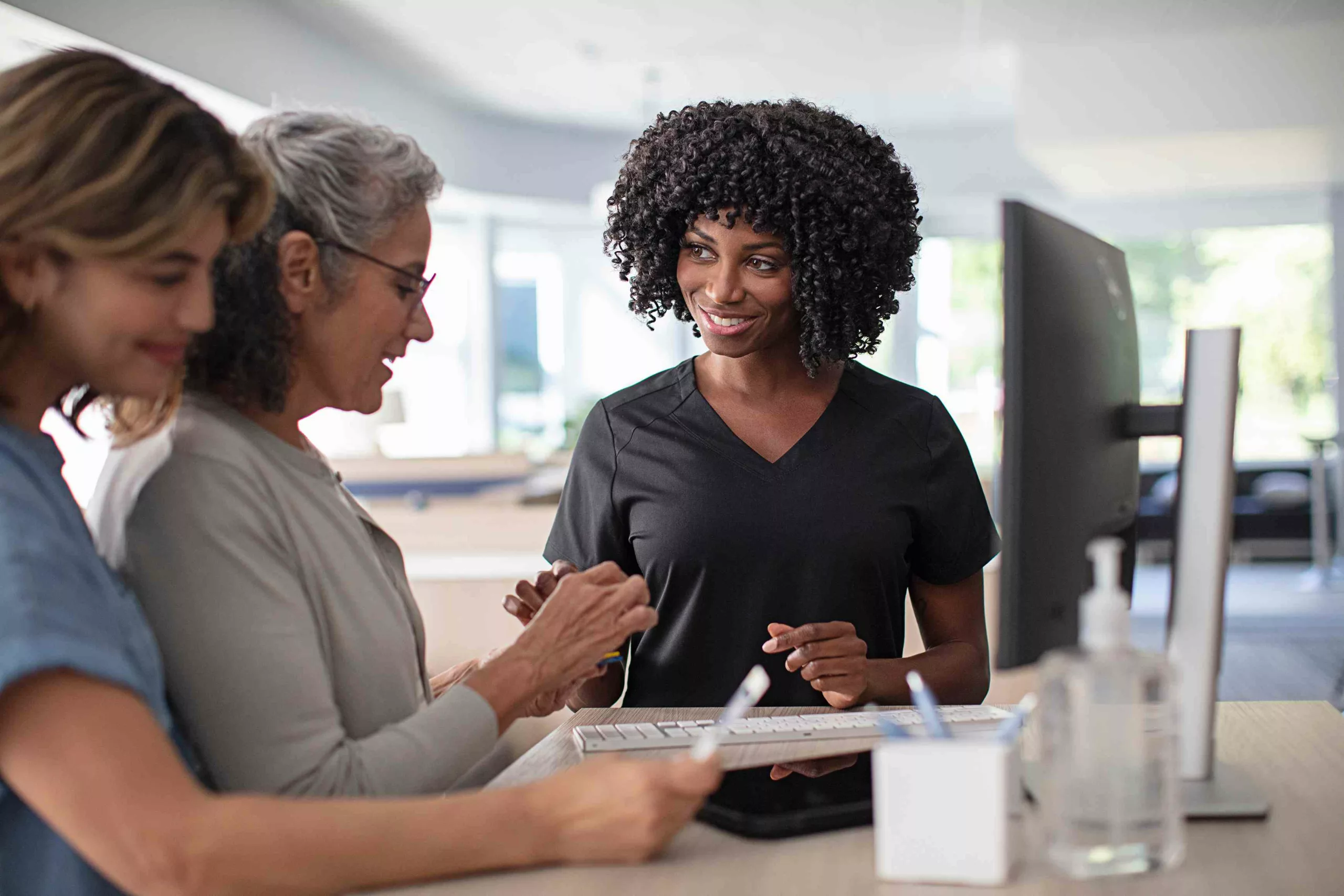 A healthcare professional consulting two patients about hearing aids in a bright clinic setting