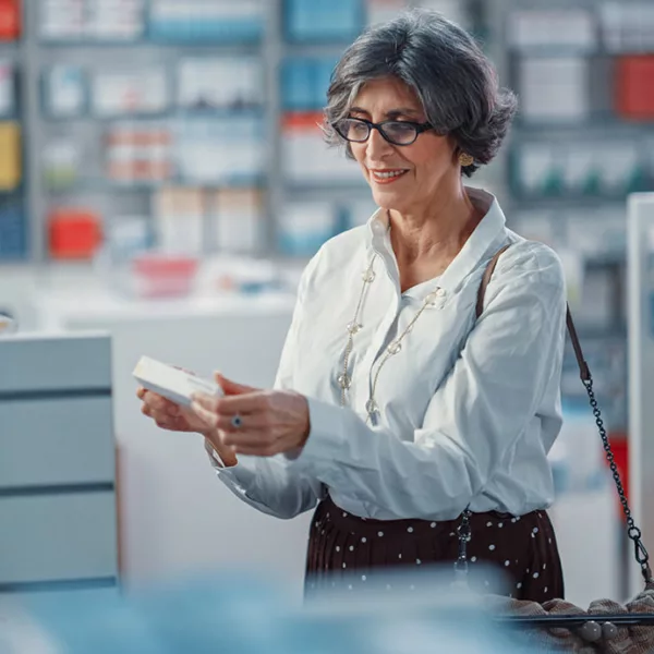 Older woman with glasses holding, and smiling at, small package in a drug store.
