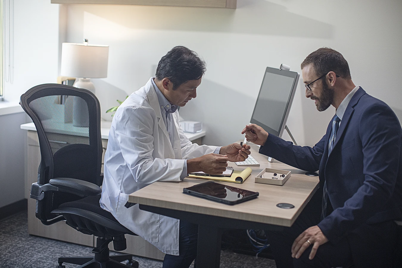 A hearing care specialist explaining The Differences Between In-the-ear and Over-the-ear Hearing Aids to a male patient at a hearing clinic