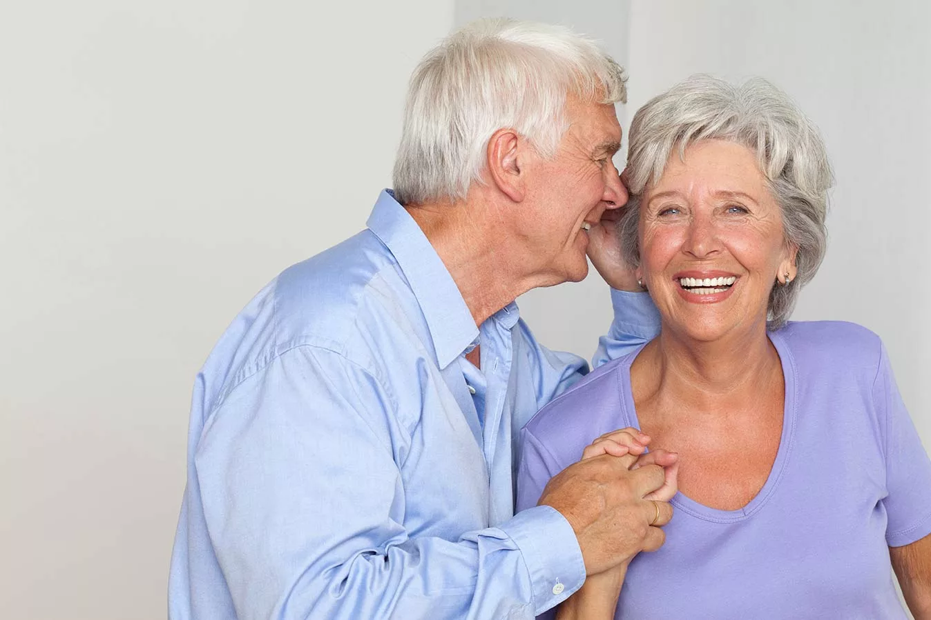 senior couple, man whispering into smiling woman's ear.