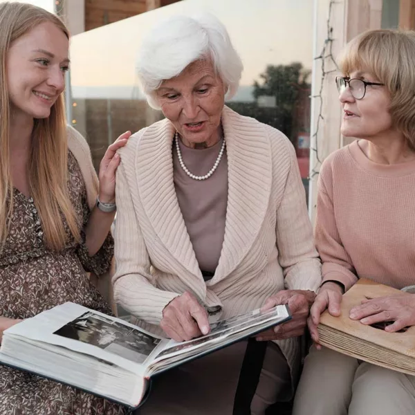 Three generations of women looking at a photo album. Middle-aged woman looks like she's straining to hear or confused.
