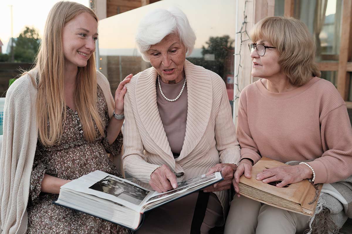 Three generations of women looking at a photo album. Middle-aged woman looks like she's straining to hear or confused.