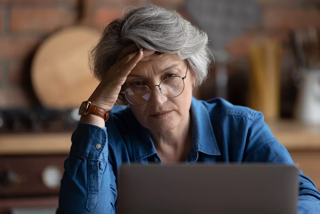 woman with hand on her forehead looking confused at laptop