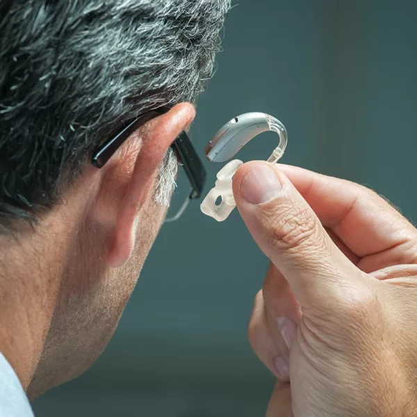 Close up of the side profile of an older man with gray hearing trying to put in a hearing aid
