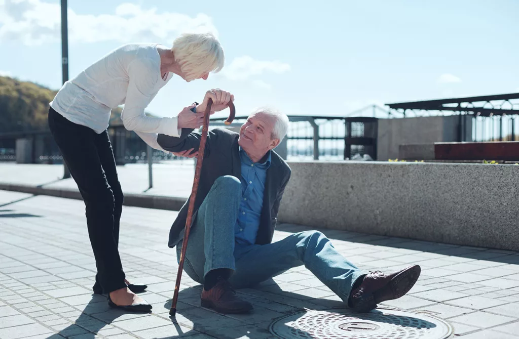 senior man with cane being helped up by senior woman in a public walkway