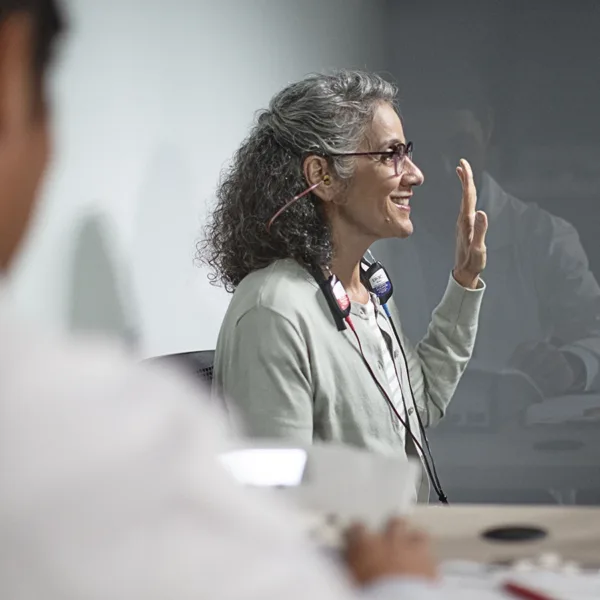 A woman sitting in a soundproof both with her hand raised as she takes a hearing test during a hearing aid consultation at a hearing clinic