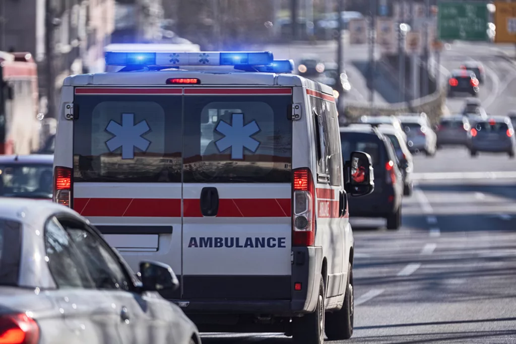 Ambulance with lights on crossing lanes on busy freeway. 