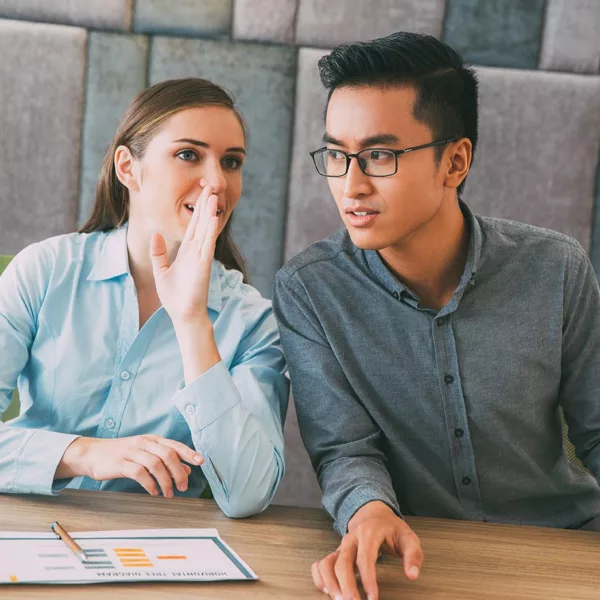 woman whispering with flat hand to mouth while man leans toward her to hear