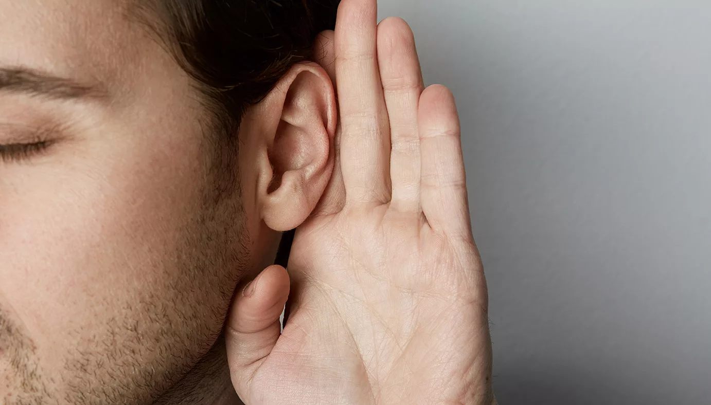 close up of man with sideburns and short hair with eyes closed and hand held behind ear