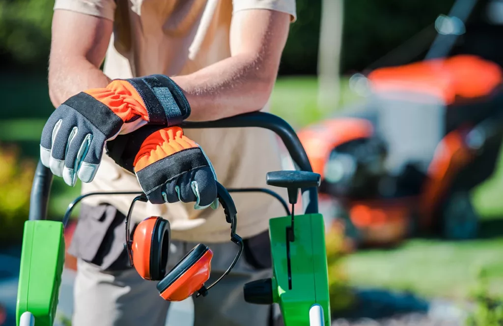 Landscape worker holding professional hearing protection while standing next to power tools