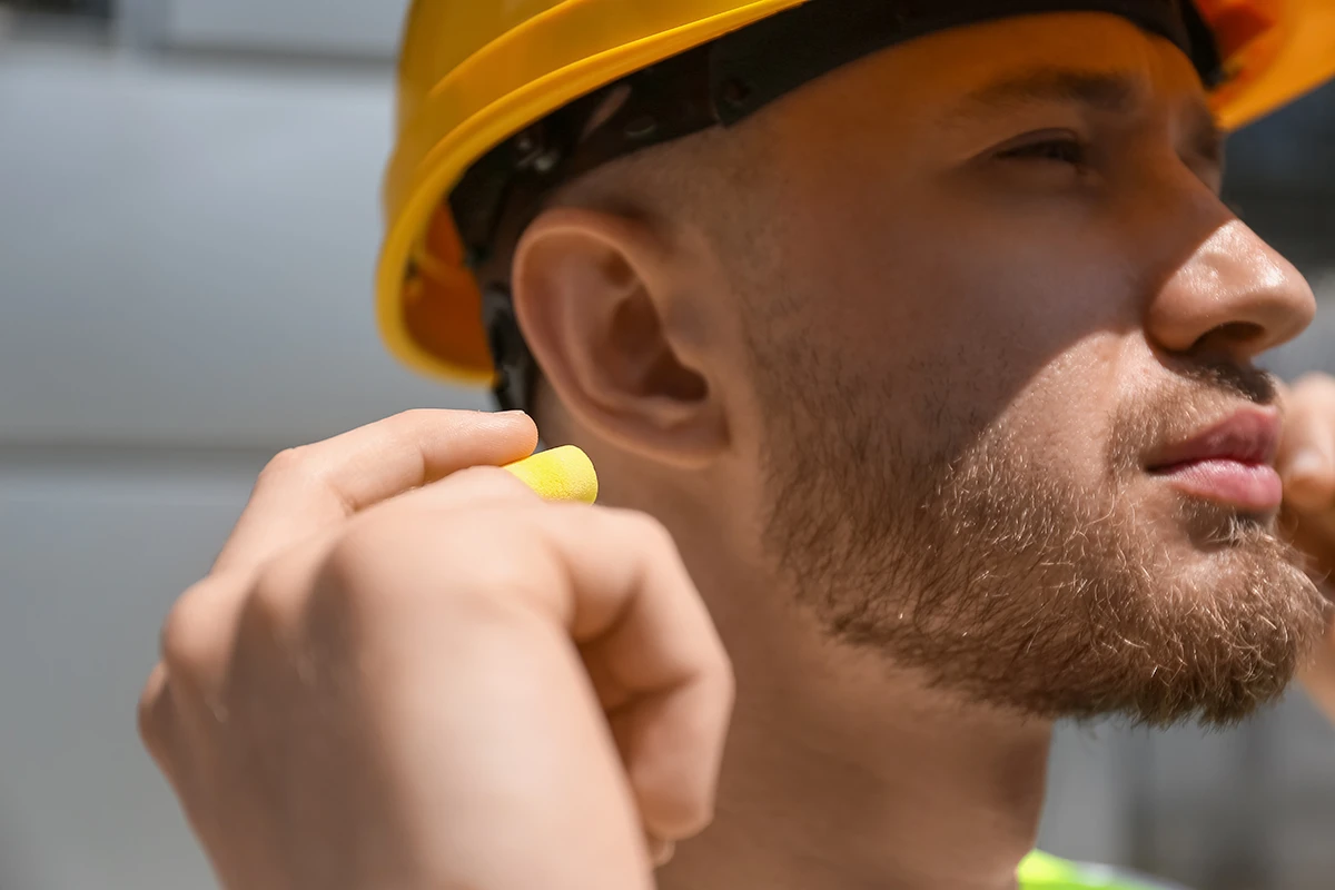 Male worker putting ear plug outdoors, closeup