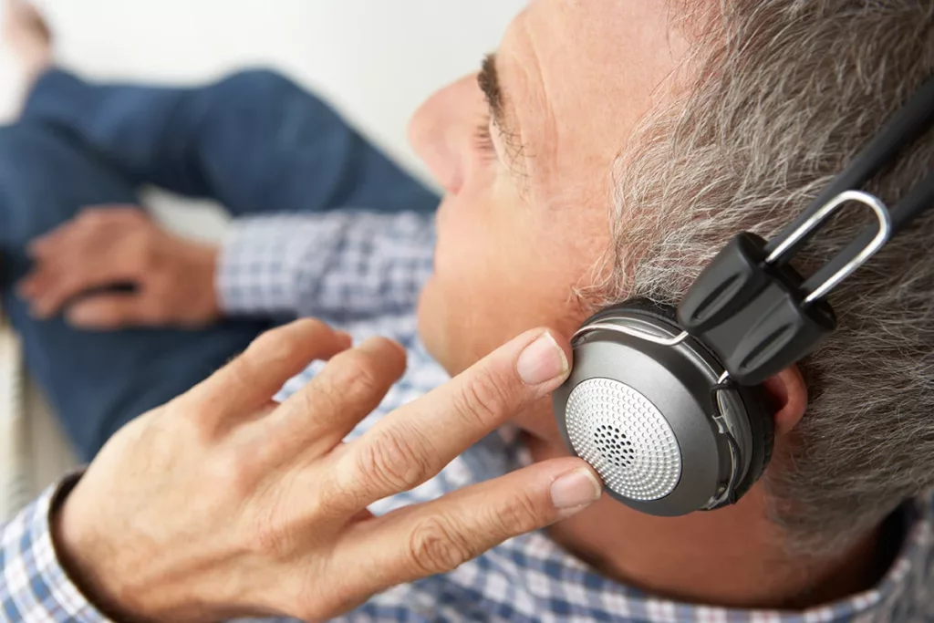 A middle aged man sitting down listen to music on headphones