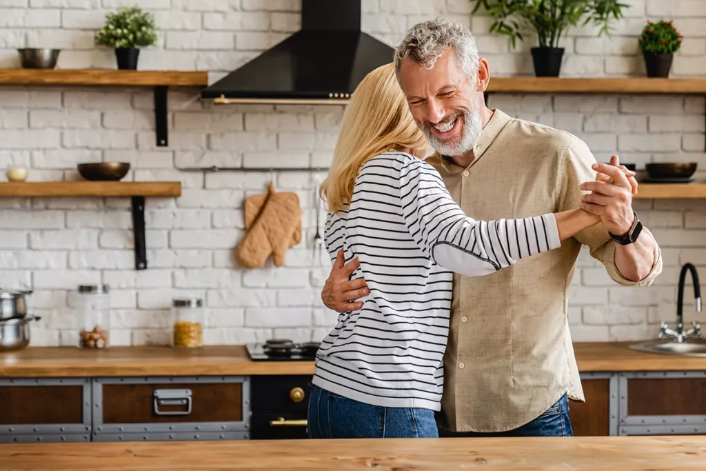 A happy and healthy middle aged couple playfully dancing in their kitchen