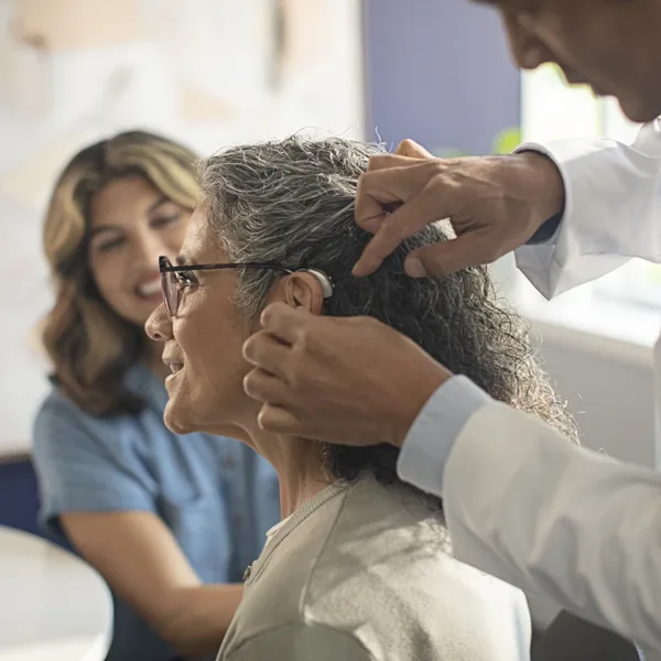 The side profile of a woman in an a hearing clinic as her hearing care specialists fits a new hearing aids in her ear