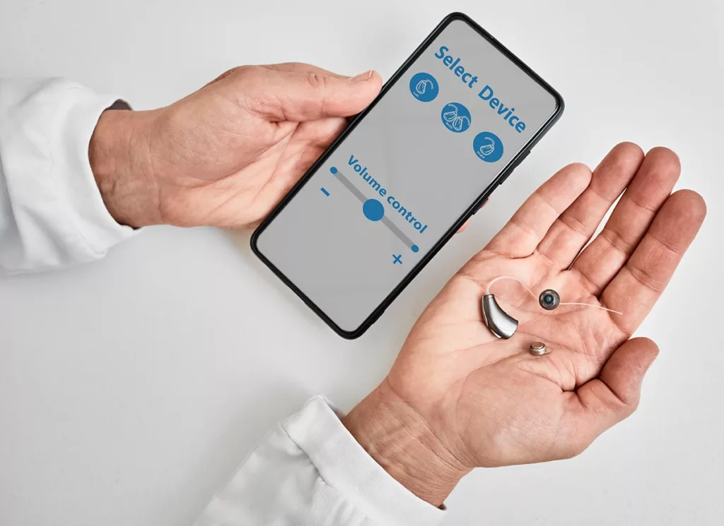 A hearing care specialist holding a Bluetooth hearing aid while pairing it with a smartphone