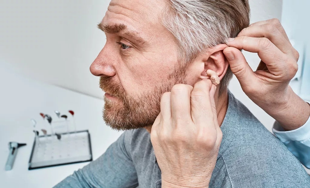 Hearing healthcare specialist inserting a discreet hearing aid in adult man's ear at a hearing clinic.