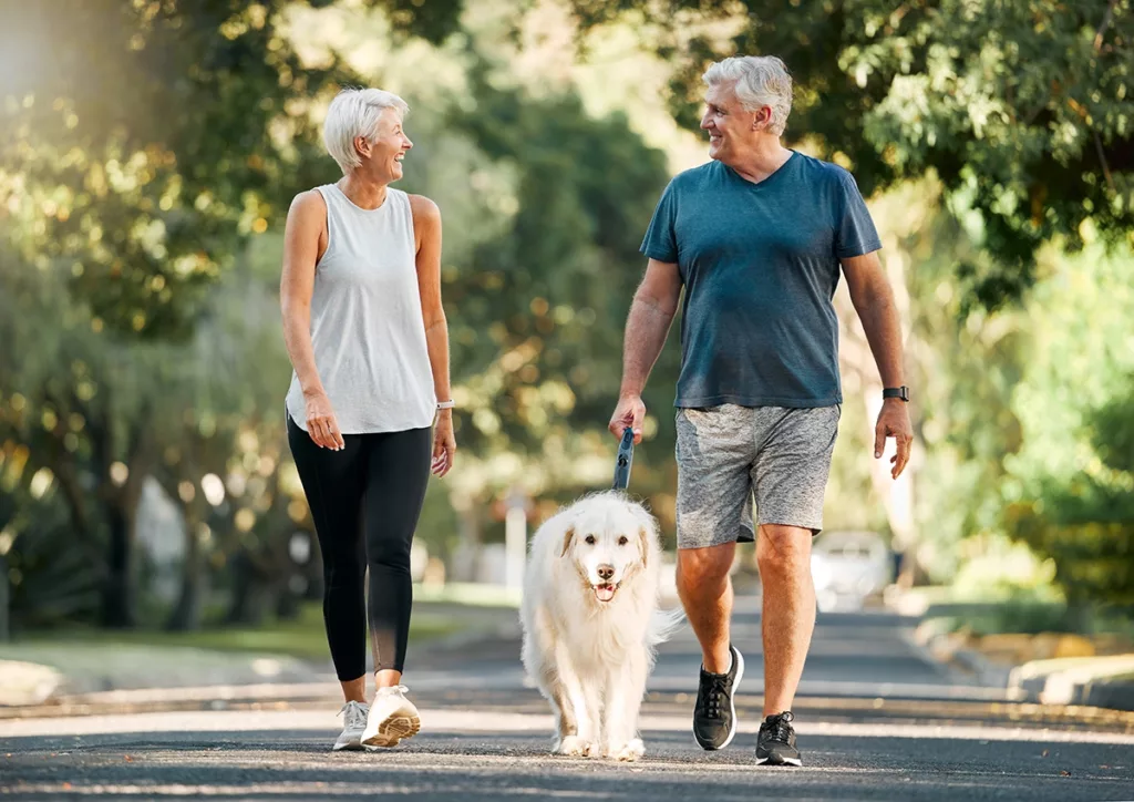 Healthy and happy senior couple walking together through a beautiful neighborhood park with their dog 