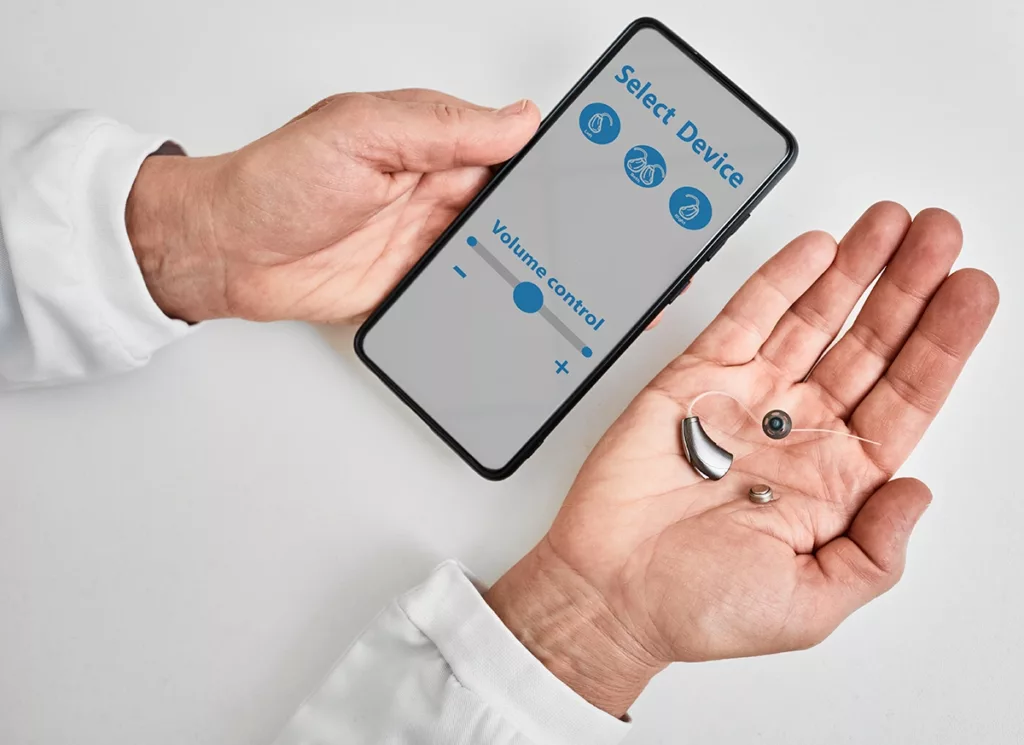 A hearing healthcare specialist holding a Bluetooth hearing aid while pairing it with a smartphone app 