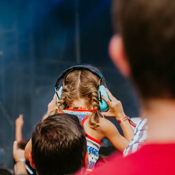 A young person at a loud rock music concert wearing cute blue ear muffs to prevent noise induced hearing loss