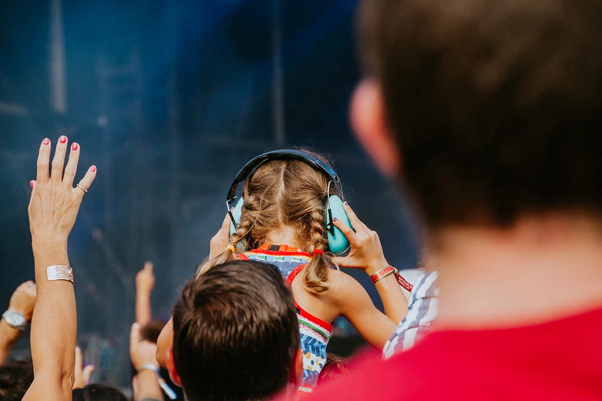 A young person at a loud rock music concert wearing cute blue ear muffs to prevent noise induced hearing loss