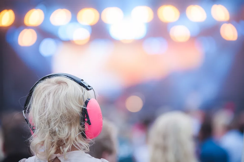 A young child wearing appropriately sized ear muffs at a loud event to protect their ears from noise induced hearing loss