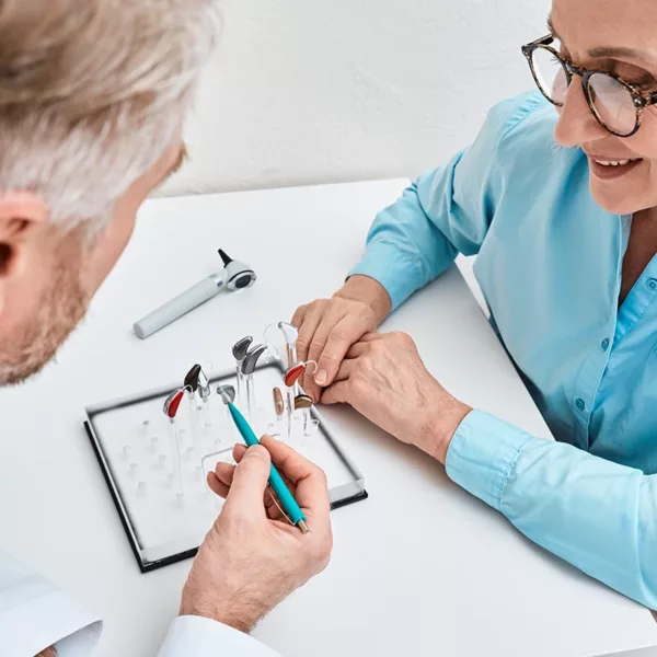 A hearing care specialist explaining various hearing aid styles to a patient at a hearing clinic