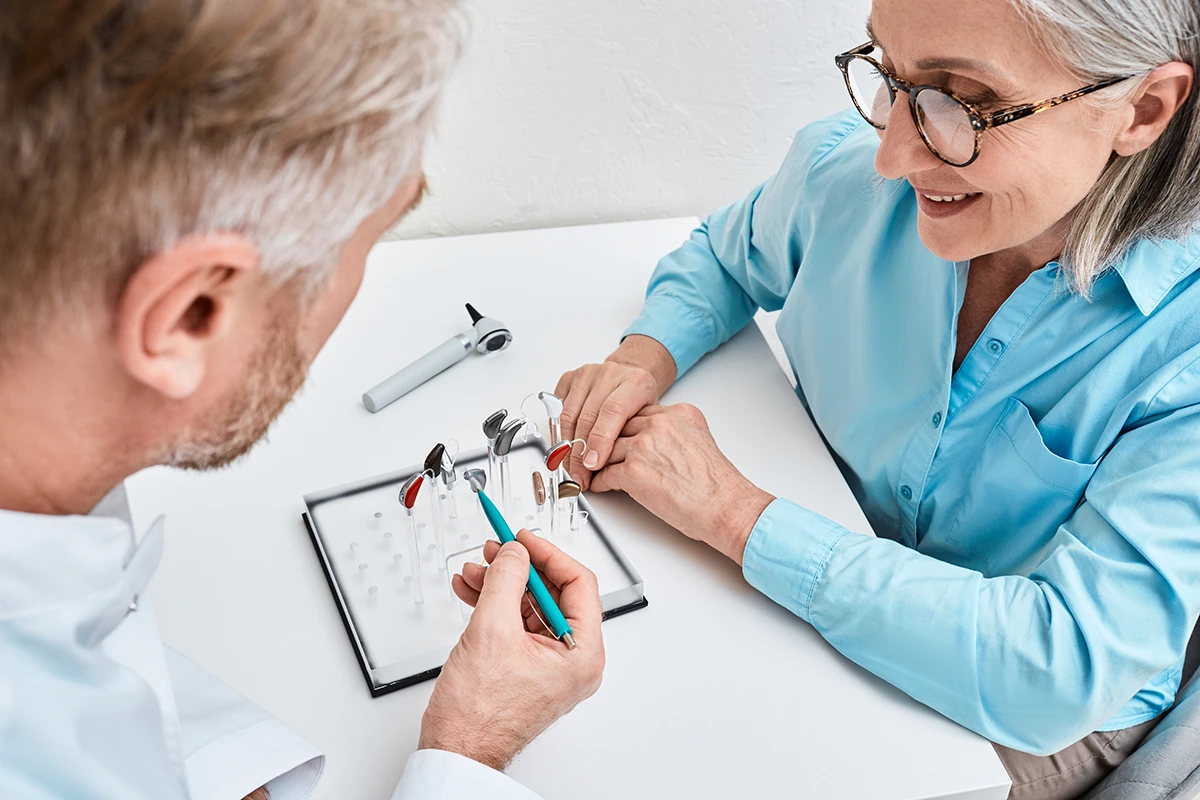 A hearing care specialist explaining various hearing aid styles to a patient at a hearing clinic
