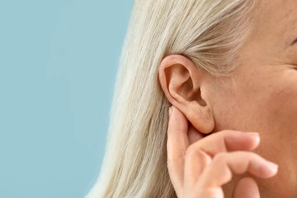 Close up of an older adult women with sensorineural hearing loss, holding her hand to her ear to try and hear better
