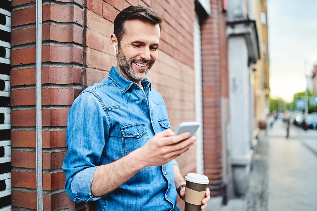 Man video calling on his smartphone using wireless noise-canceling headphones outside on a city street