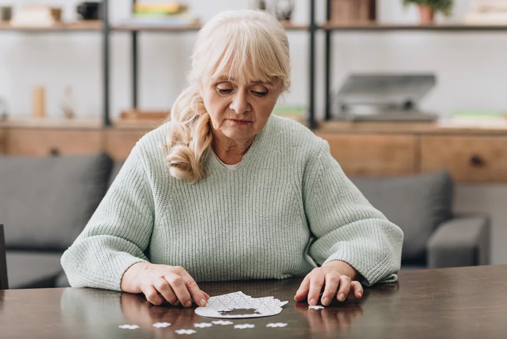 An older woman experiencing cognitive decline does a puzzle on a table.