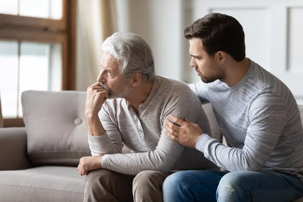 An older man with untreated hearing loss sits on a couch with his son.