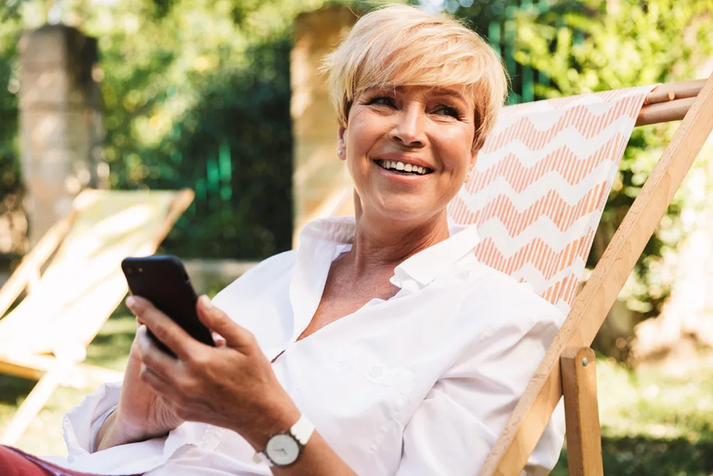 Happy mature women on vacation, on her smartphone, using a hearing aid app for traveling 