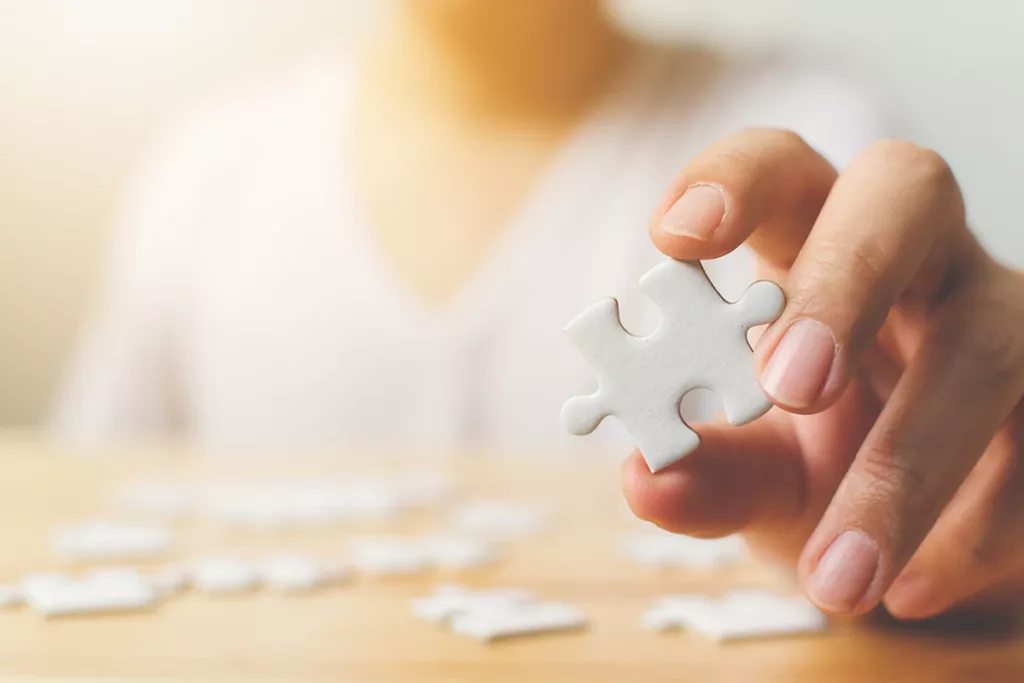 A hand holding up a puzzle piece, in focus at the forefront, with a blurry background, symbolying the connection between hearing loss and dementia. 