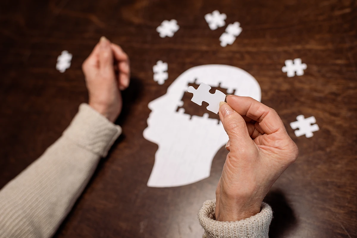 Older adult women doing a puzzle in the shape of a human brain, symbolizing the connection between hearing loss and dementia.