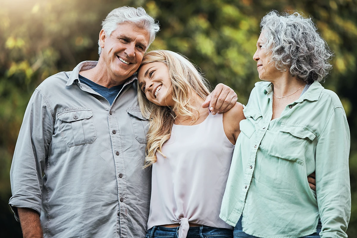 An adult daughter loving hugging her senior aged mother and father while enjoying time together as a family, symbolizing caring for a loved one with hearing loss