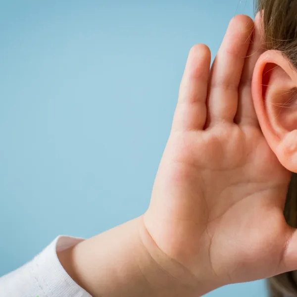 A close up of a small child holding their hand up to their ear as if to help them hear better, symbolizing hereditary hearing loss.