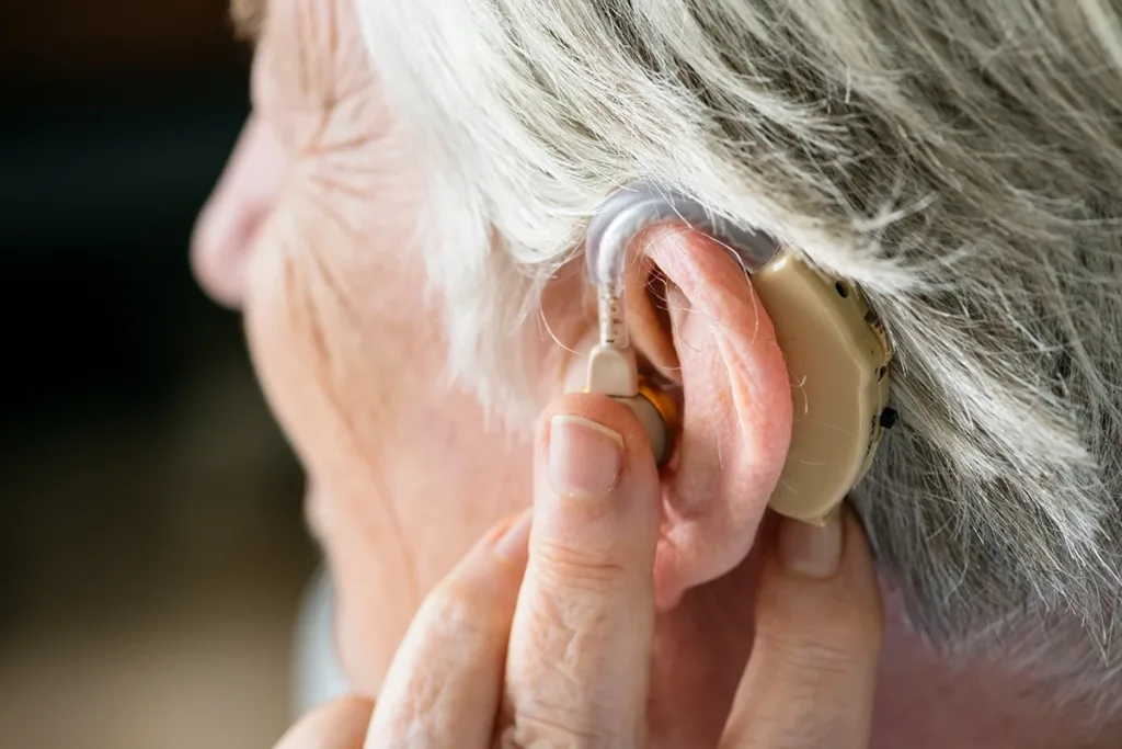 A close up side profile of an older person putting in an over-the-counter otc hearing aid