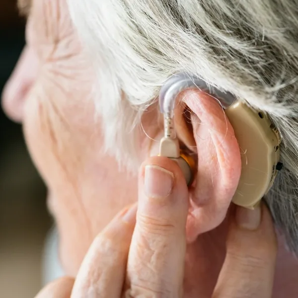 A close up side profile of an older person putting in an over-the-counter otc hearing aid