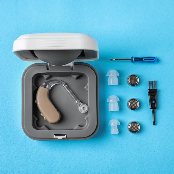 A BTE hearing aid in a case with hearing aid cleaning supplies placed next to it on a blue background