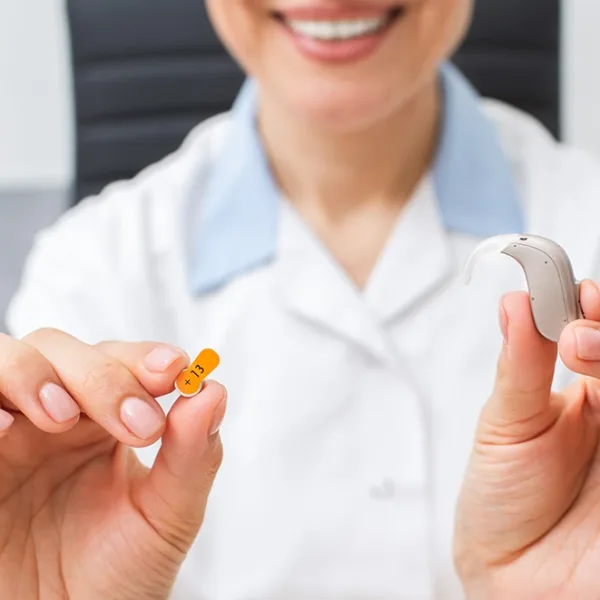 A hearing care specialist holding up a BTE hearing aid and an Orange , size 13 hearing aid battery