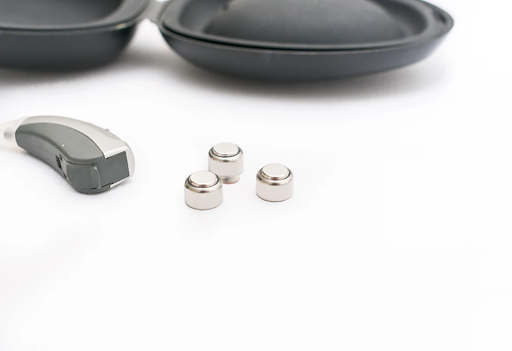 A BTE hearing aid with three hearing aid batteries on a white background