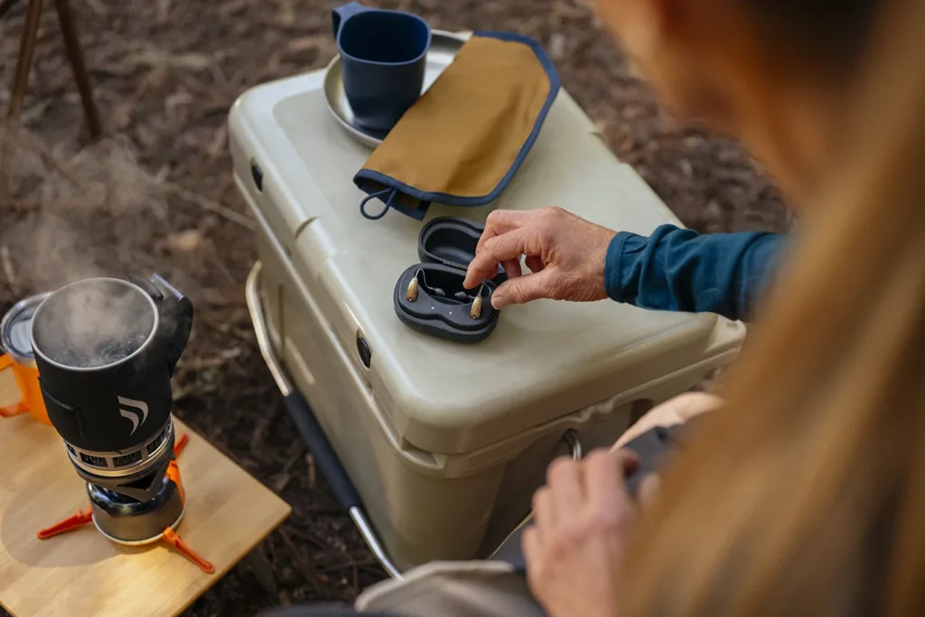 A woman taking a rechargeable hearing aid out of it's charging case.