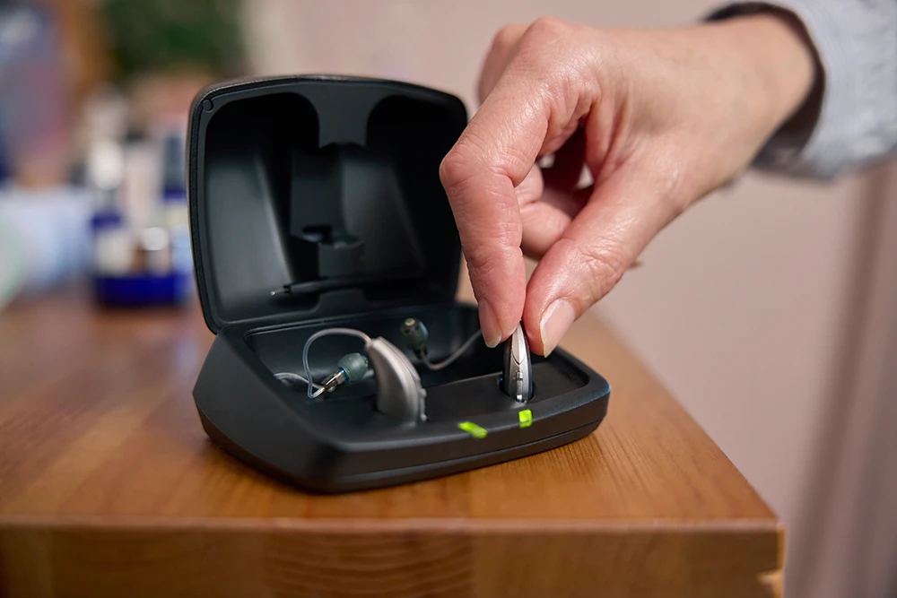 Close up ofa. person picking up their rechargeable hearing aids from the charging case on their nightstand